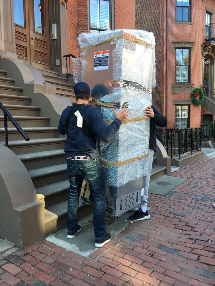 Small Haul crew carrying a shrink-wrapped appliance down brick steps