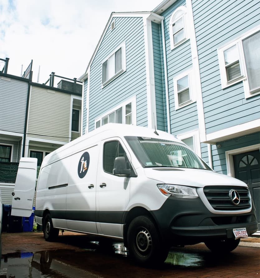 A white Small Haul Mercedes Sprinter cargo van parked outside a Boston triple-decker