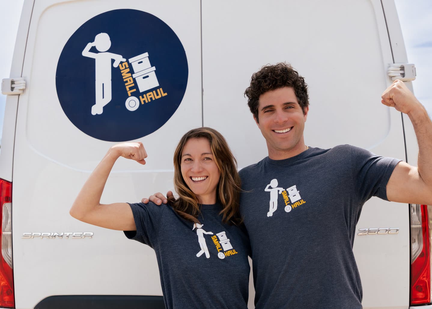 Two Small Haul team members flexing in branded tees in front of a Sprinter van