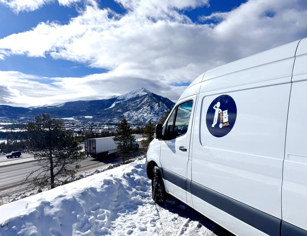 A Small Haul Sprinter van parked on a snowy Colorado roadside beneath the mountains